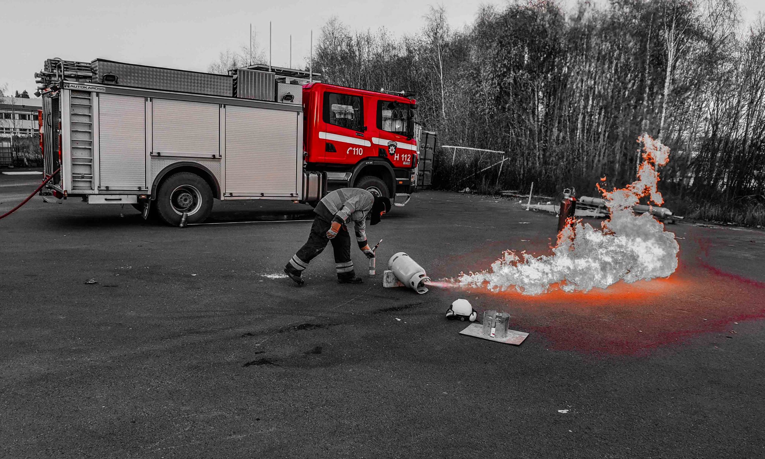 Sort-hvitt b ilde av en brannkonstabel ved en brennende gassflaske, med en brannbil i bakgrunnen