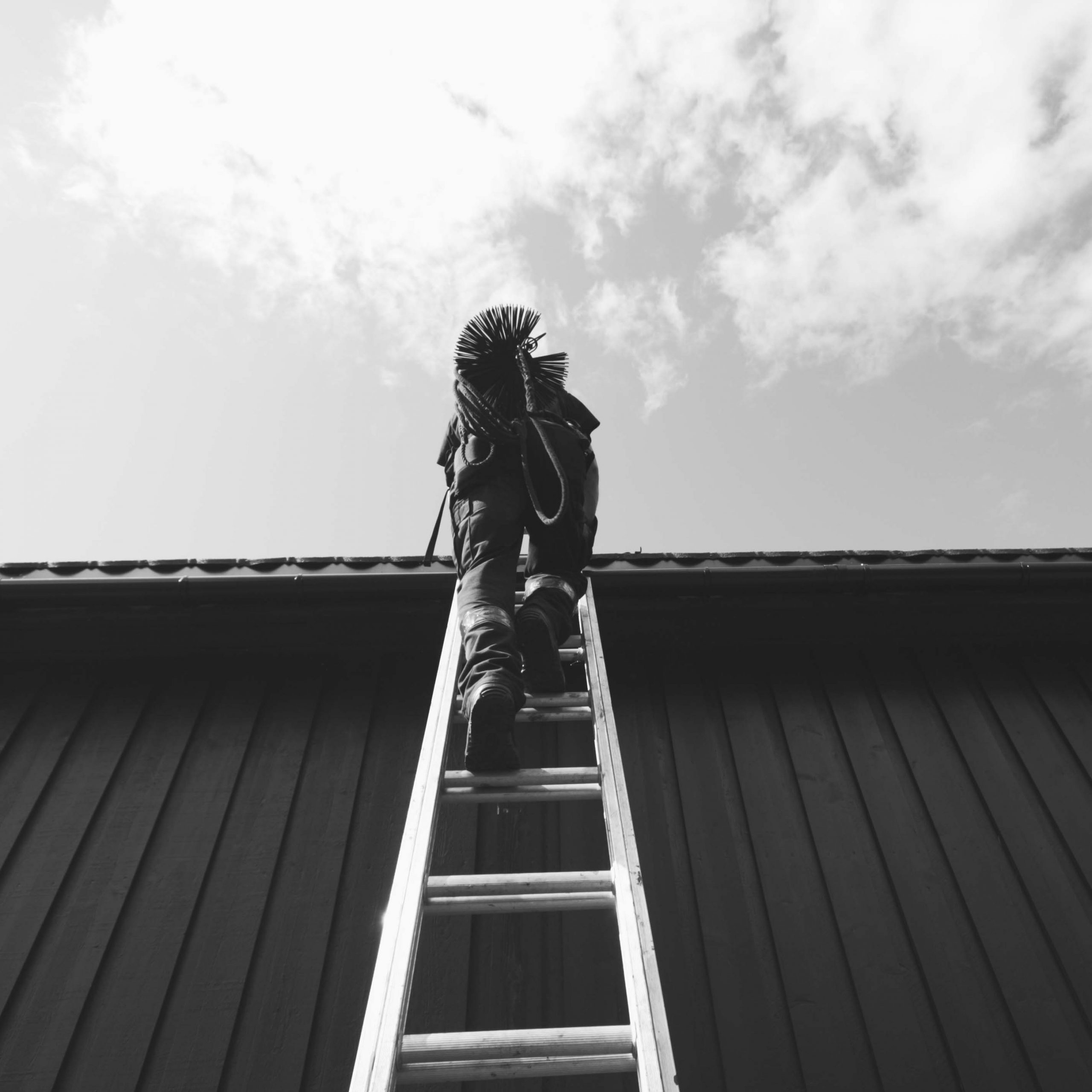 Sort-hvitt bilde av en brannforebygger på vei opp en stige til et tak