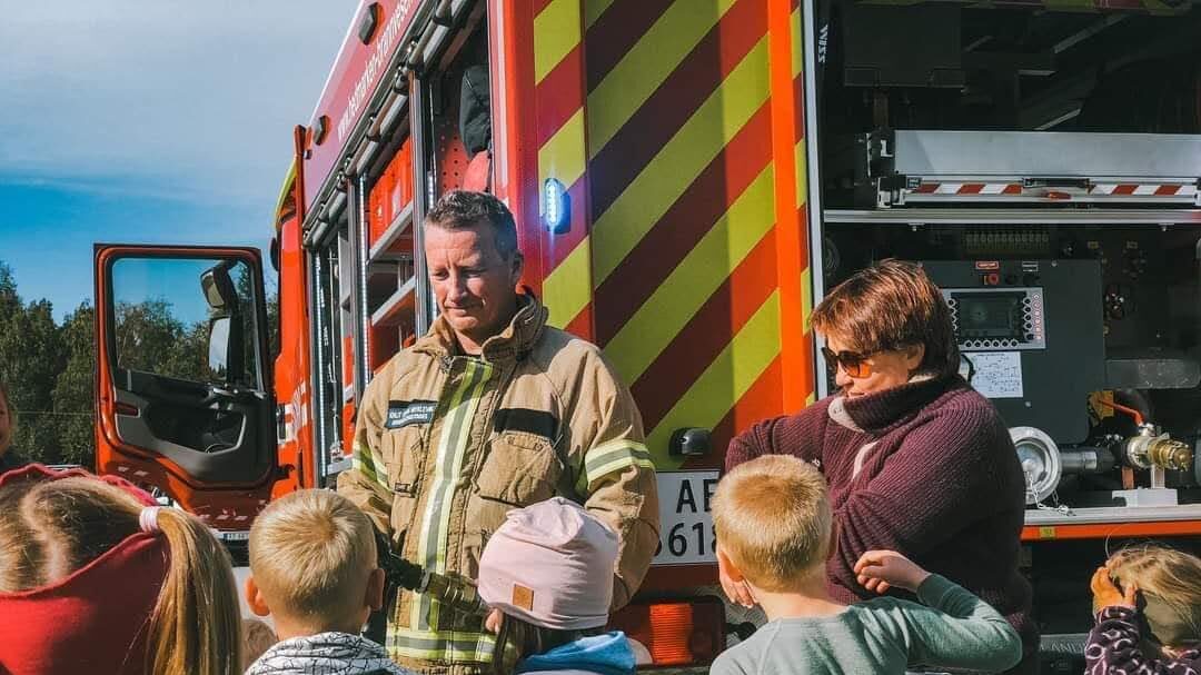 Brannkonstabel som snakker med barn foran en brannbil